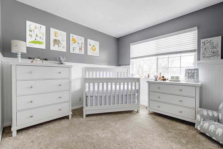 دکوراسیون اتاق خواب نوزاد مدرن با دیوار خاکستری، پرده کرکره ای و تخت نوزاد سفید که سرتاسر کف آن موکت کرم پهن شده است